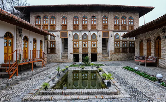 خانه شیرنگی با نمای آجری و درب وپنجره های چوبی و حوض در وسط محوطه سنگ فرش شده 5452