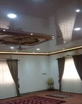 فرش قرمز و پرده های سفید قهوه ای و سقف نور پردازی شده با نور سفید سالن نشیمن ویلا در گمیشان